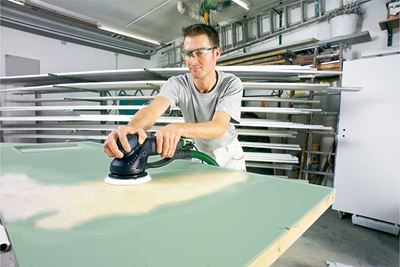 A man sands a surface that is painted green